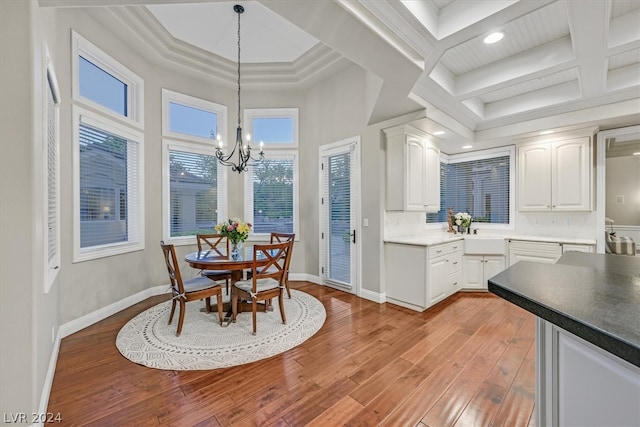 kitchen with coffered ceiling, light hardwood / wood-style flooring, a notable chandelier, tasteful backsplash, and white cabinets