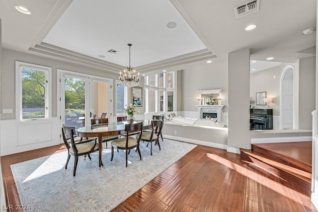 dining area with a notable chandelier, wood-type flooring, and a raised ceiling