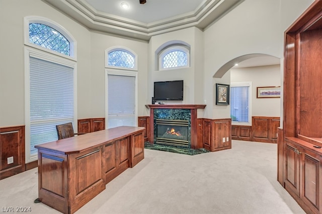 office with a premium fireplace, light colored carpet, a towering ceiling, and a tray ceiling