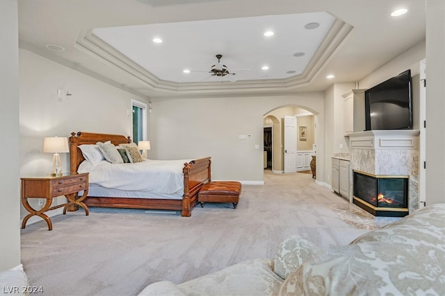 bedroom with a tray ceiling, a multi sided fireplace, carpet flooring, and ceiling fan