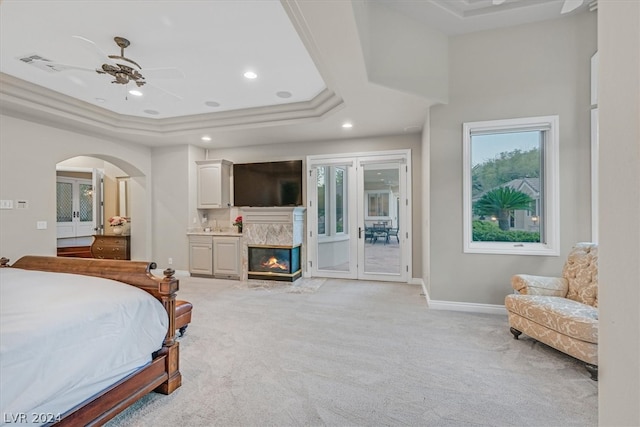 bedroom with a premium fireplace, access to outside, ceiling fan, a tray ceiling, and light colored carpet