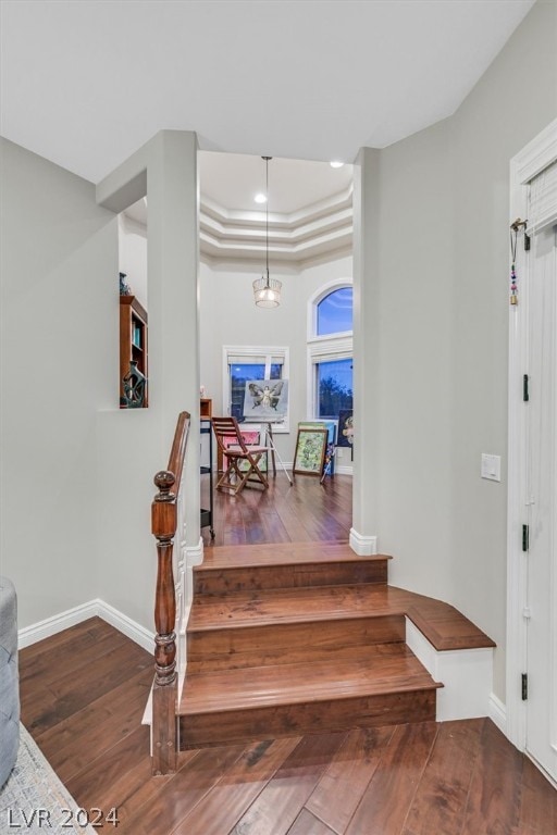 staircase with a raised ceiling, crown molding, and wood-type flooring