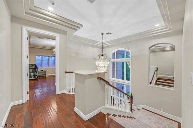 hallway featuring dark hardwood / wood-style flooring, crown molding, a notable chandelier, and a raised ceiling