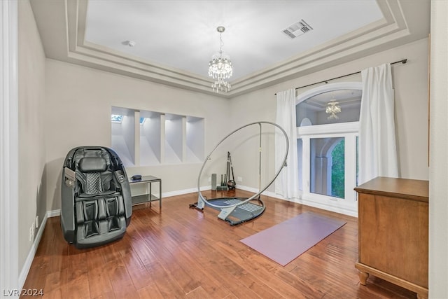 exercise room featuring a chandelier, hardwood / wood-style flooring, and a raised ceiling