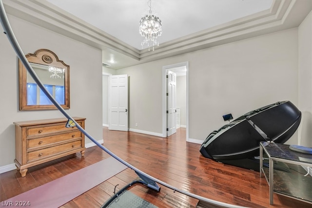 workout area featuring an inviting chandelier, dark hardwood / wood-style flooring, and a tray ceiling