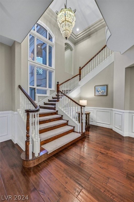 stairs with ornamental molding, dark hardwood / wood-style flooring, a towering ceiling, and an inviting chandelier