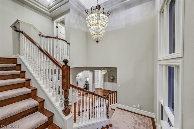 stairs featuring a towering ceiling, crown molding, and a chandelier