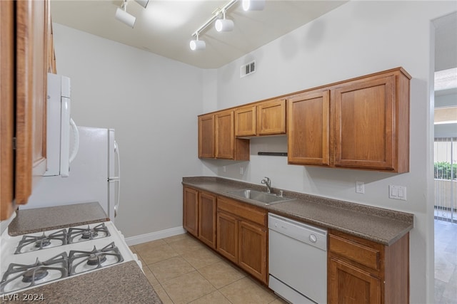 kitchen featuring white dishwasher, stove, sink, track lighting, and light tile flooring