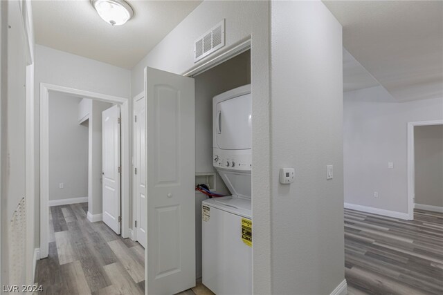 laundry area with hardwood / wood-style flooring and stacked washer / drying machine