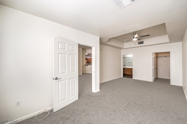 unfurnished bedroom featuring a walk in closet, ensuite bath, a closet, a raised ceiling, and carpet flooring