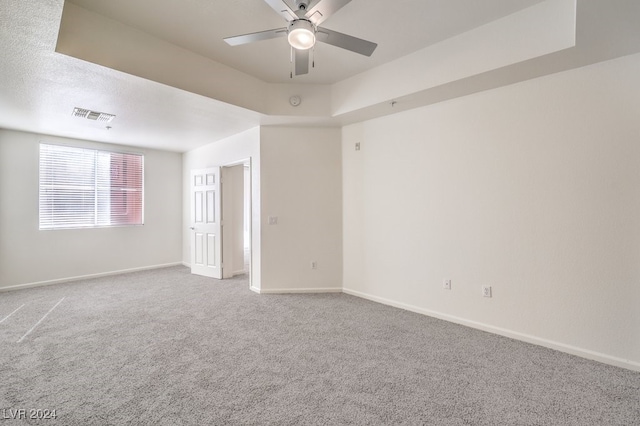 carpeted spare room with ceiling fan and a raised ceiling