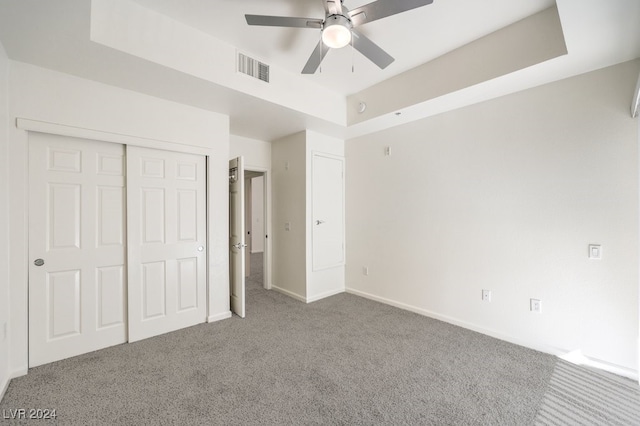 unfurnished bedroom featuring a tray ceiling, ceiling fan, carpet, and a closet