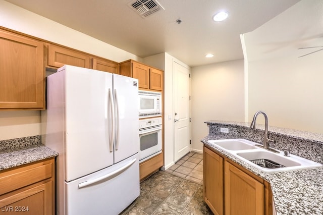 kitchen featuring sink, white appliances, and light stone counters