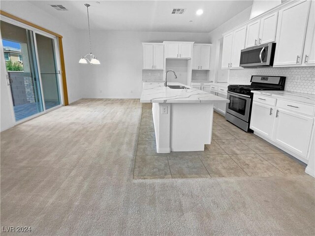 kitchen featuring decorative light fixtures, white cabinets, stainless steel appliances, and a kitchen island with sink