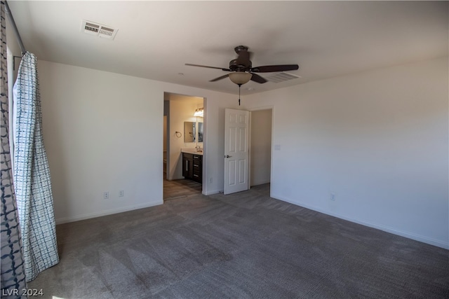 unfurnished bedroom with ceiling fan, dark colored carpet, and connected bathroom