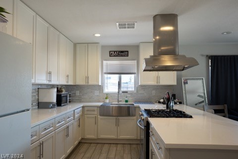 kitchen featuring appliances with stainless steel finishes, island exhaust hood, backsplash, wood-type flooring, and sink