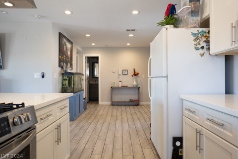 kitchen with white fridge, light wood-type flooring, blue cabinets, stainless steel gas range, and white cabinets