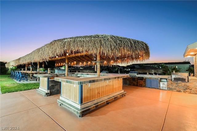 patio terrace at dusk with exterior bar, an outdoor kitchen, and grilling area