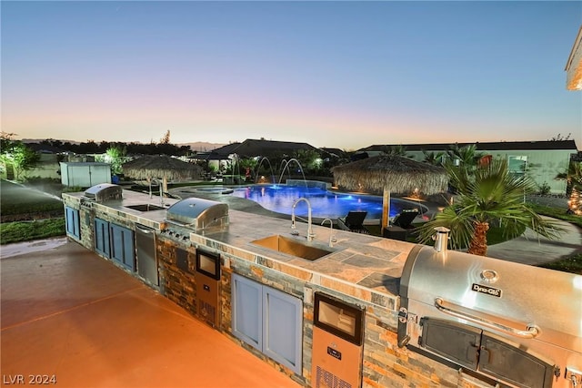 patio terrace at dusk featuring pool water feature, area for grilling, and sink