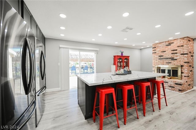 kitchen featuring light wood-type flooring, light stone countertops, a fireplace, a kitchen island, and stainless steel refrigerator