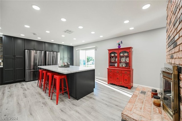 kitchen with a center island, light hardwood / wood-style floors, a breakfast bar area, and stainless steel refrigerator