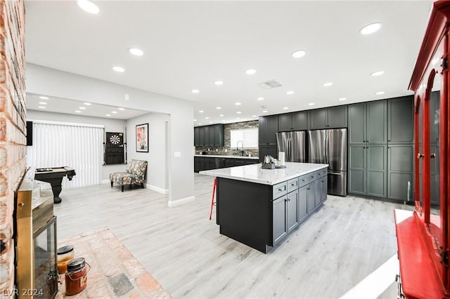 kitchen with stainless steel fridge, light wood-type flooring, light stone counters, billiards, and a center island