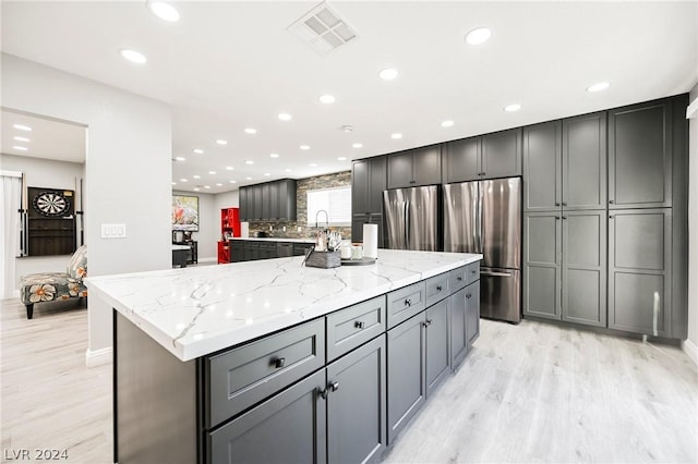 kitchen featuring gray cabinetry, stainless steel fridge, and light stone counters