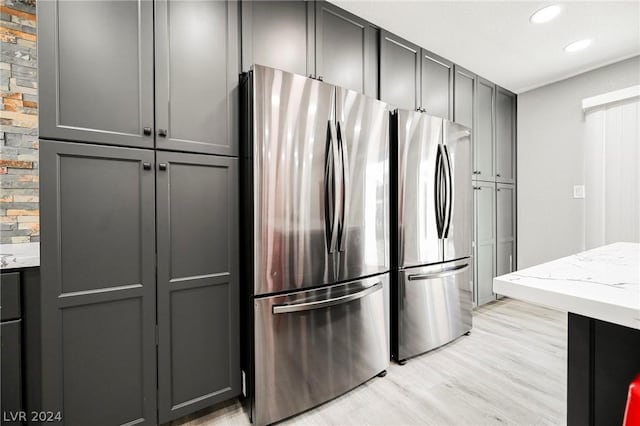 kitchen featuring stainless steel refrigerator, light stone counters, gray cabinets, and light hardwood / wood-style floors