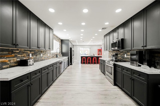 kitchen featuring light stone countertops, appliances with stainless steel finishes, backsplash, and light hardwood / wood-style flooring