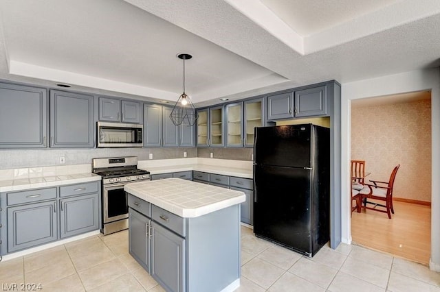 kitchen with pendant lighting, tile countertops, a center island, a raised ceiling, and appliances with stainless steel finishes