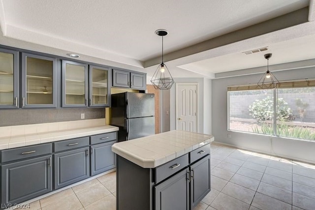 kitchen with black refrigerator, light tile patterned floors, a center island, and decorative light fixtures