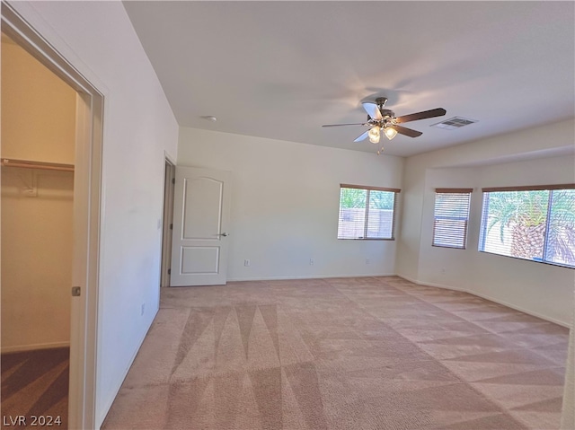 unfurnished bedroom with light colored carpet, a spacious closet, ceiling fan, and a closet