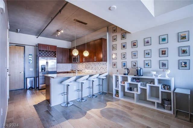 kitchen with kitchen peninsula, stainless steel appliances, backsplash, hardwood / wood-style flooring, and pendant lighting