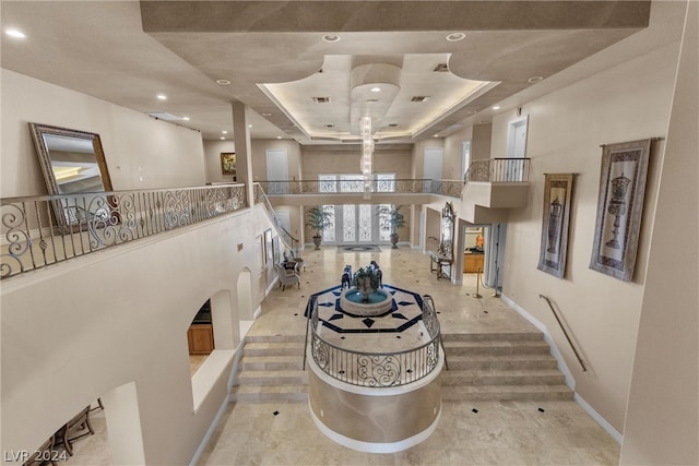 hallway with a towering ceiling, a tray ceiling, and light tile patterned floors