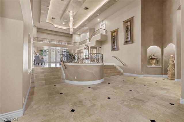 corridor featuring light tile patterned flooring, a towering ceiling, and a tray ceiling