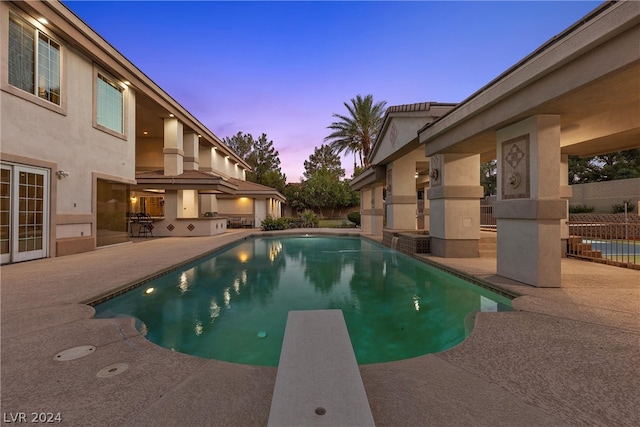 pool at dusk with a diving board and a patio