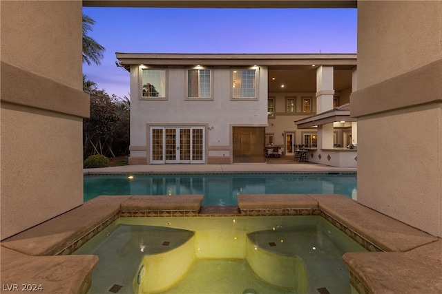 pool at dusk featuring a patio and an in ground hot tub