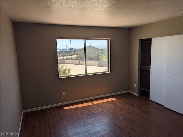 unfurnished bedroom featuring a textured ceiling, dark wood-type flooring, and a closet