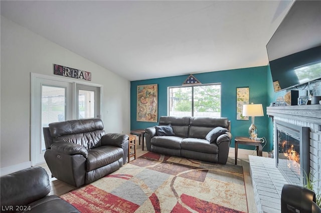 living room with a brick fireplace, vaulted ceiling, and wood-type flooring