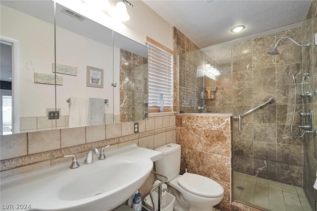 bathroom with a textured ceiling, tasteful backsplash, an enclosed shower, and sink