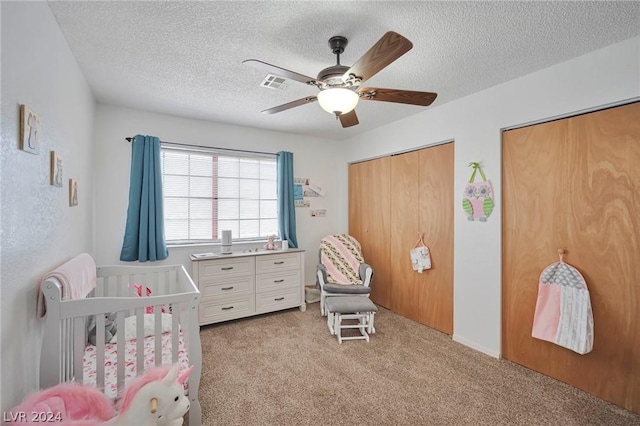 bedroom featuring a textured ceiling, ceiling fan, light carpet, and a crib