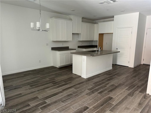 kitchen featuring white cabinets, dark hardwood / wood-style flooring, an island with sink, and an inviting chandelier