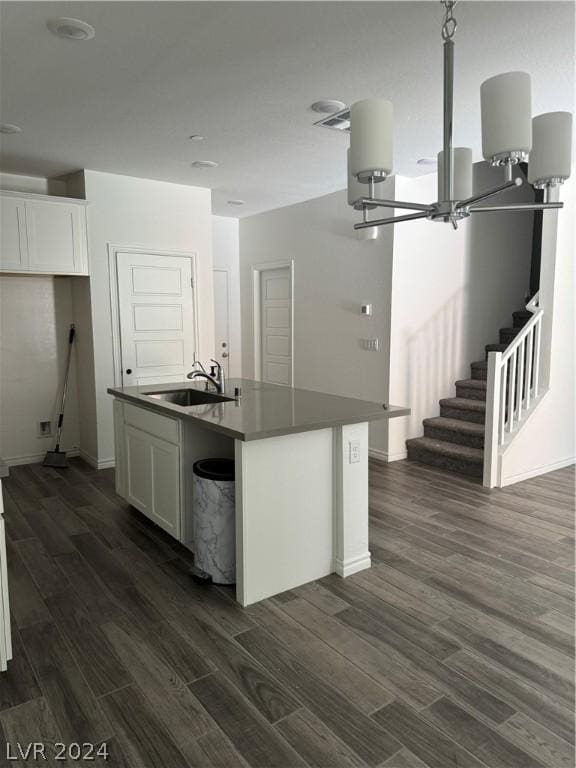 kitchen featuring dark hardwood / wood-style flooring, sink, a center island with sink, an inviting chandelier, and white cabinets