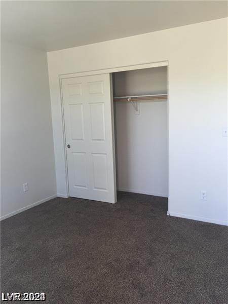 unfurnished bedroom with dark colored carpet and a closet