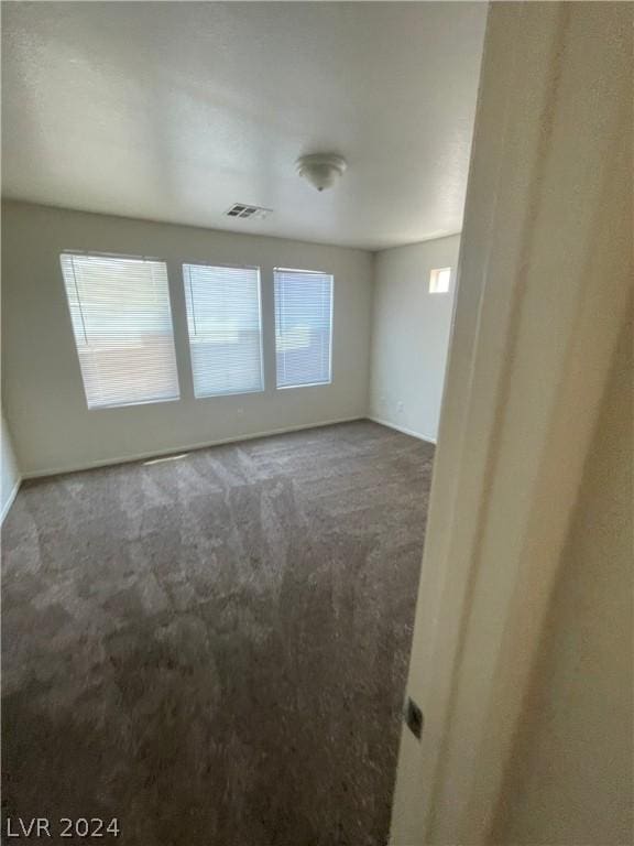 empty room featuring dark colored carpet and a wealth of natural light