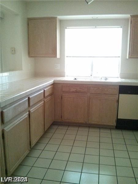 kitchen featuring light tile patterned flooring, tile counters, dishwasher, and a wealth of natural light