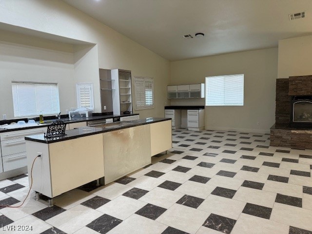 kitchen with a kitchen island, high vaulted ceiling, sink, a fireplace, and white cabinets