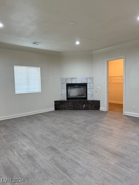 unfurnished living room featuring ornamental molding, a stone fireplace, and hardwood / wood-style floors