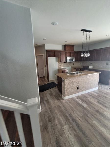 kitchen featuring a center island with sink, sink, tasteful backsplash, decorative light fixtures, and wood-type flooring