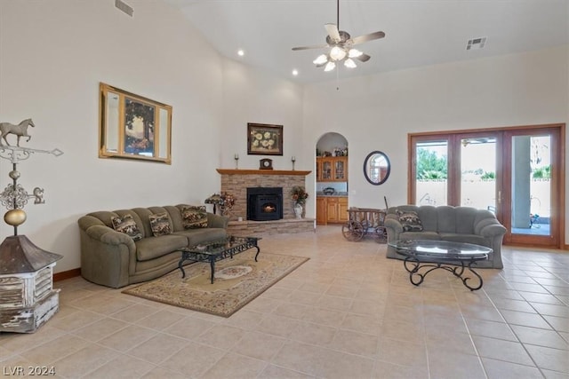 tiled living room featuring ceiling fan, a stone fireplace, and a high ceiling